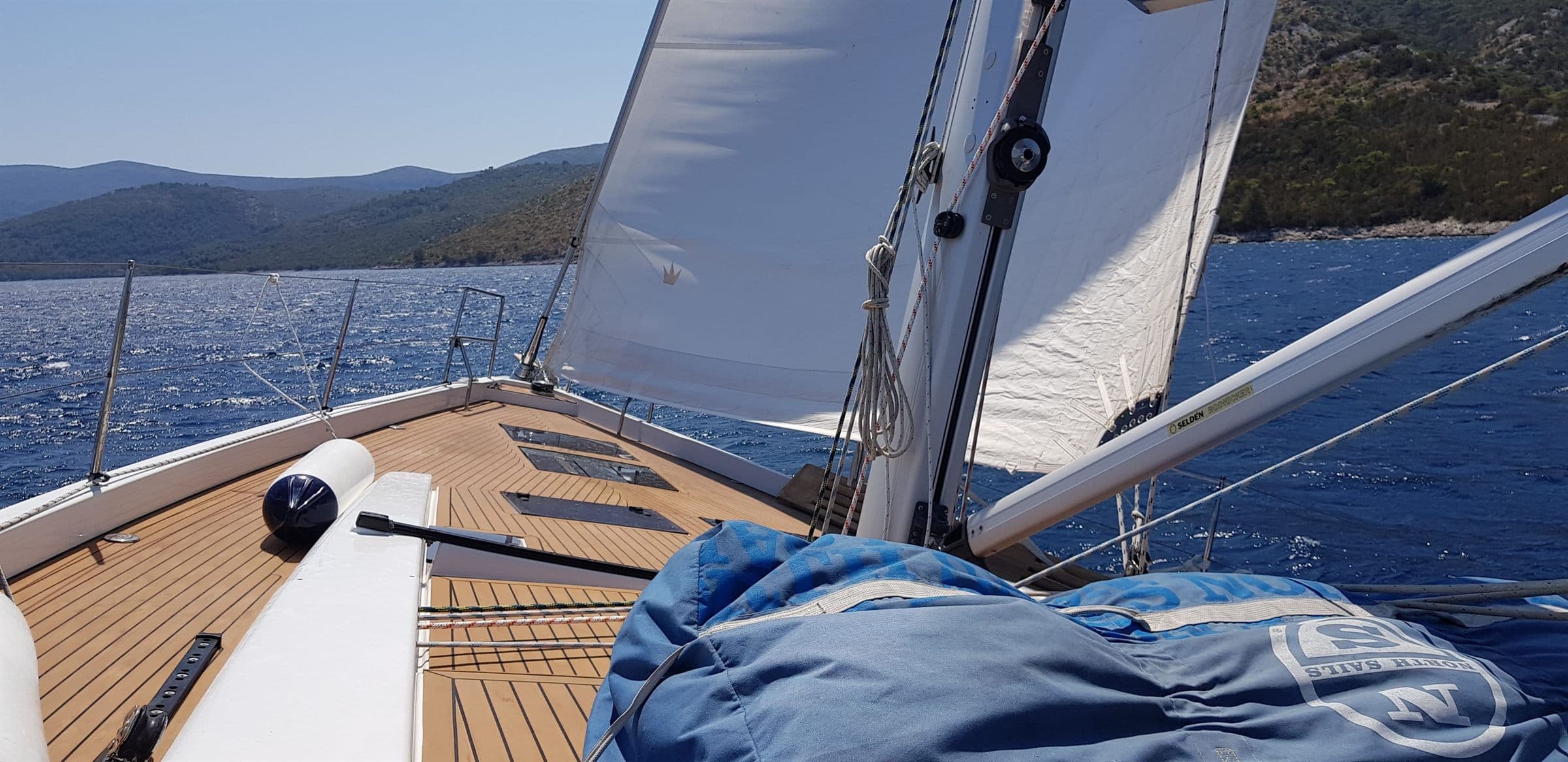 The teak foredeck of a sailing yacht under sail, the coast ahead