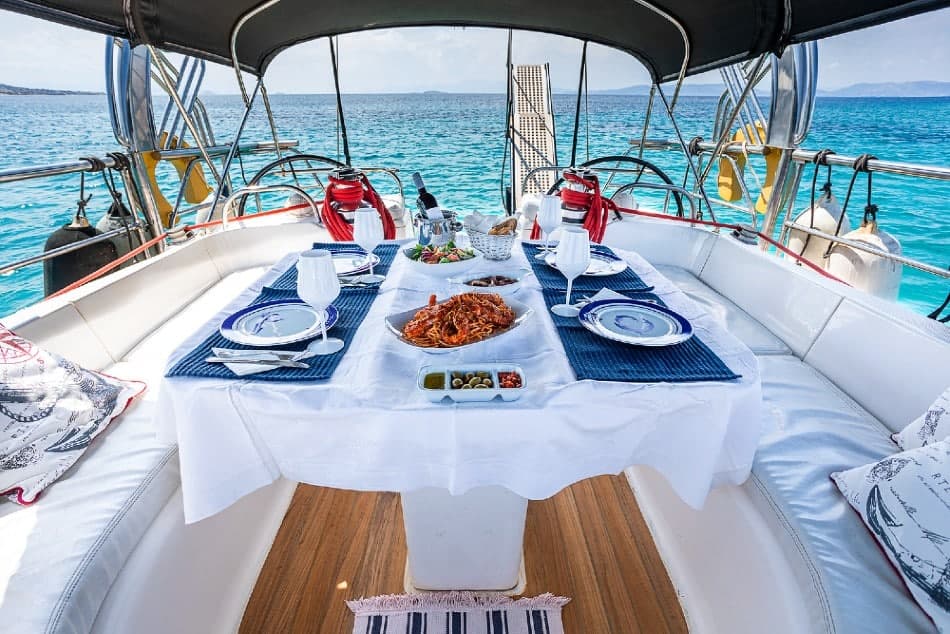 A table laid for lunch under the bimini of a sailing yacht, with turquoise sea beyond