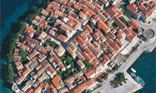 Aerial view of Korčula's walled old town on its small peninsula, its streets laid out in a herringbone around the cathedral