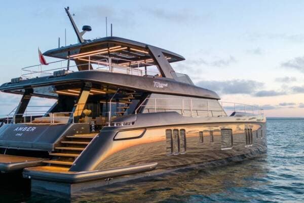 A large power catamaran at dusk, its decks lit
