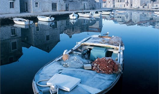 A wooden fishing boat loaded with nets lying in a still stone harbour on Hvar, houses reflected in the water