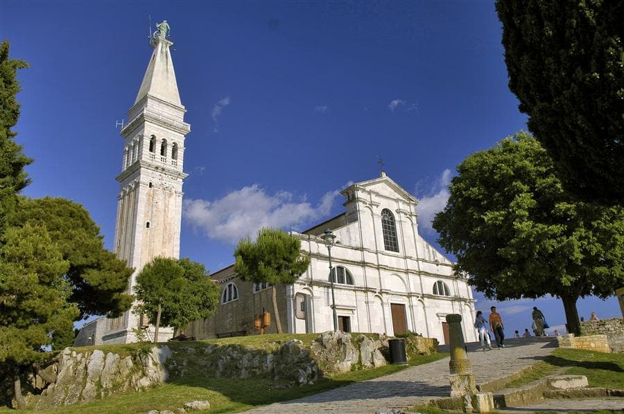 The church of St Euphemia and its tall campanile at the top of Rovinj, framed by pines against a deep blue sky