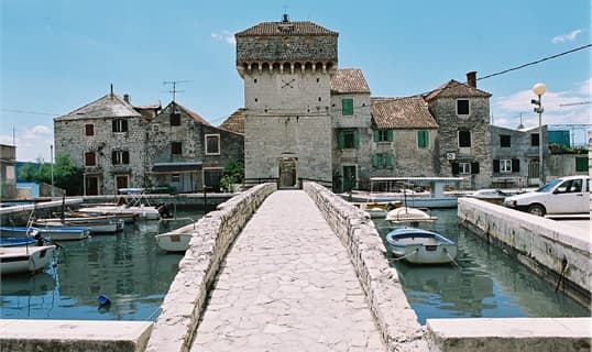 The fortified stone village of Kaštel Gomilica reached by a causeway, with small boats moored on either side