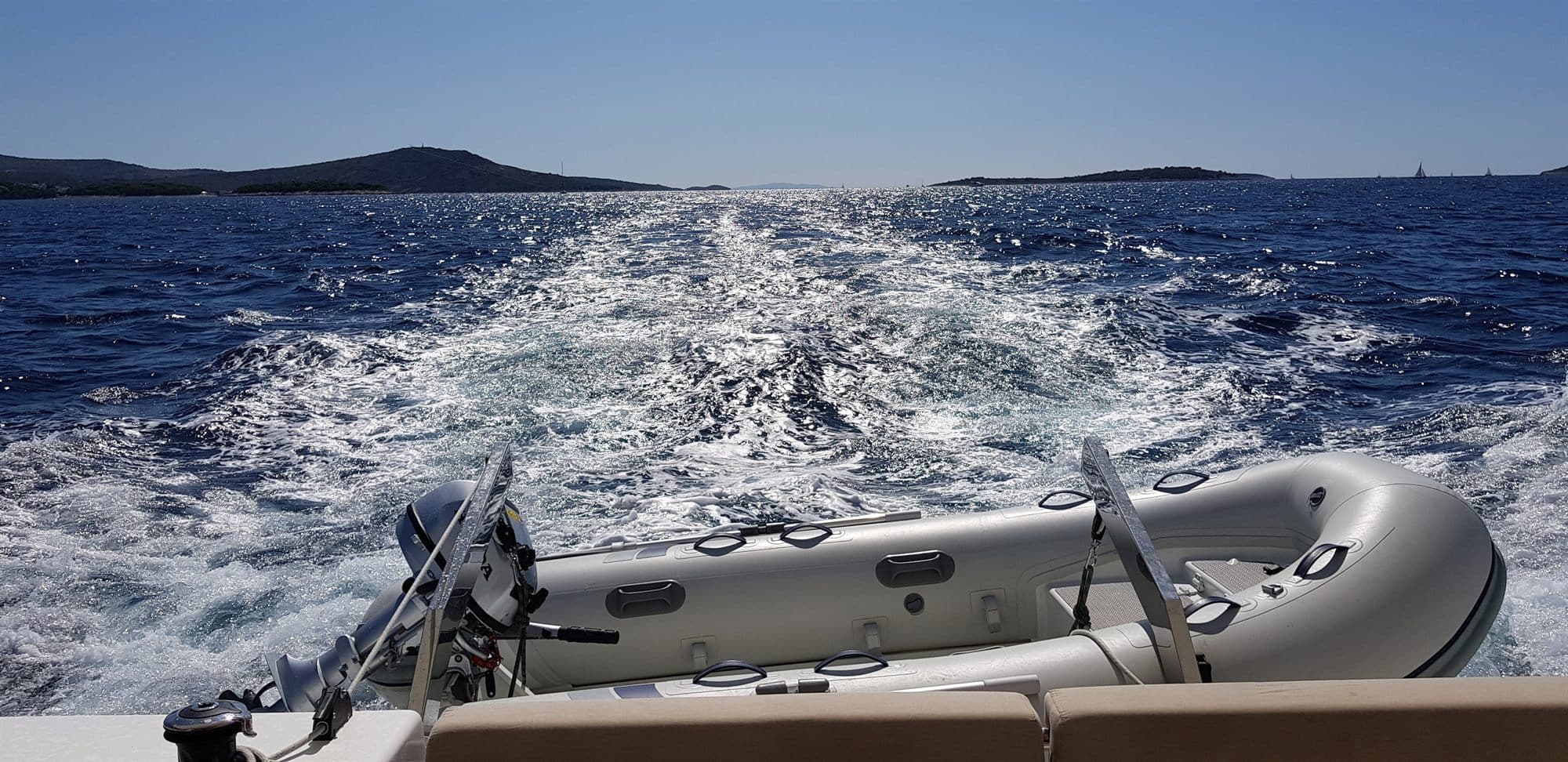 An inflatable tender towed astern across a broad wake, with low Croatian islands on the horizon