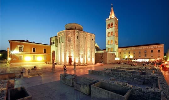 The round church of St Donatus and its bell tower lit at dusk, standing on the stones of the Roman forum in Zadar